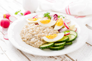 Oatmeal porridge with boiled egg and vegetable salad with fresh radish, cucumber and lettuce. Healthy dietary breakfast