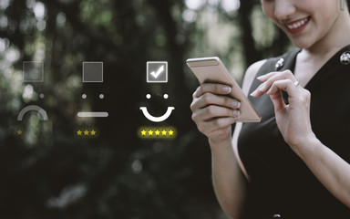 Businesswoman pressing face emoticon on virtual touch screen at smartphone .Customer service...