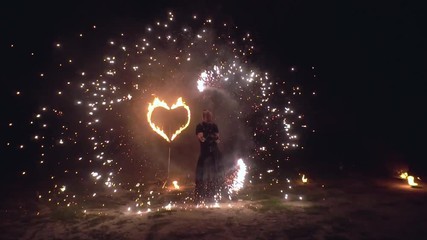 Man artist twist fire objects in his hands sparkling fire show with burning heart on background