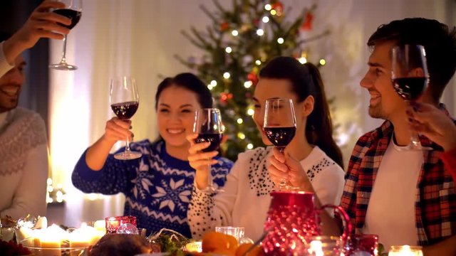 holidays and celebration concept - happy friends having christmas dinner party at home, drinking red wine and clinking glasses