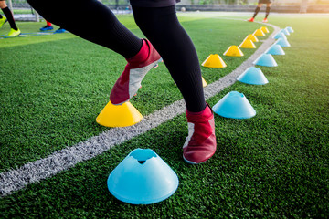 Soccer player Jogging and jump between cone markers on green artificial turf for soccer training. - Powered by Adobe