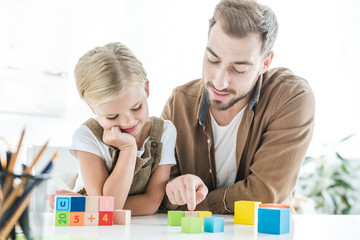 happy father and little daughter learning mathematics with colorful cubes at home