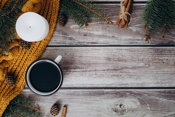 Cup of coffee  , candle, bumps, cinnamon, spruce branches and warm orange scarf on wooden table. Winter concept. Flat lay, top view. 