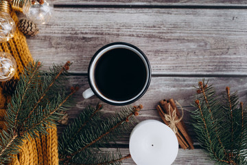 Cup of coffee  , candle, bumps, cinnamon, spruce branches and warm orange scarf and decorated with led lights  on wooden table. Winter concept. Flat lay, top view. 
