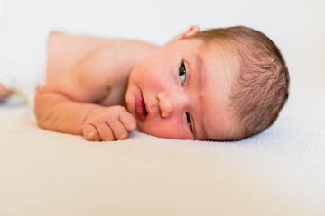 Portrait of pretty newborn girl lying on her bed and looking at the camera.