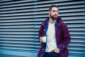 Handsome young man in purple winter jacket drinking coffee. The guy drinking coffee on the street.