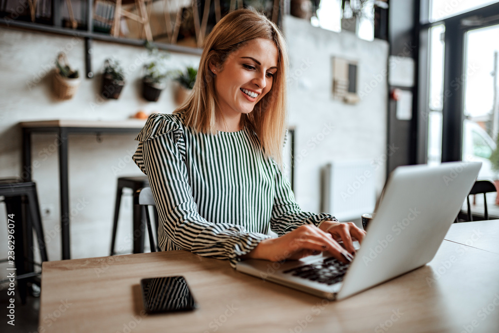 Wall mural Smiling woman typing on laptop indoors.