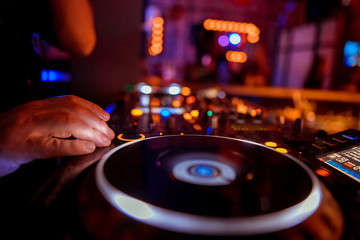 Dj mixes the track in the nightclub at party. Headphones in foreground and DJ hands in motion