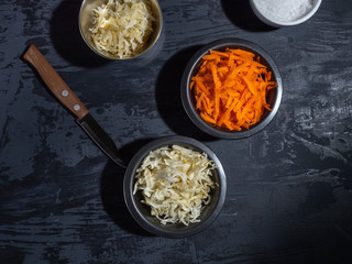 Billet for salad, sliced carrot cabbage in black plates, grated cheese