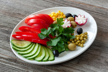 Vegetarian food: chopped vegetables consist of tomatoes, cucumbers, radishes with olives, greens, corn and green peas on a white plate