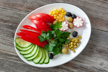 Vegetarian food: chopped vegetables consist of tomatoes, cucumbers, radishes with olives, greens, corn and green peas on a white plate