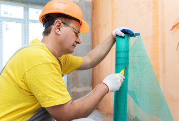 The worker is cutting  a fiberglass mesh.