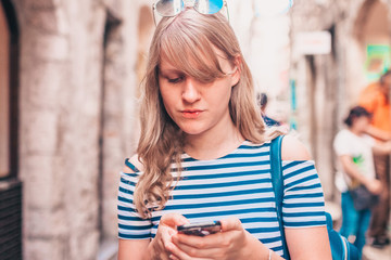 Attractive trendy urban cute blonde is using a smartphone on a city street