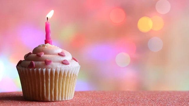 Birthday cupcake and candle on colorful defocused background party concept