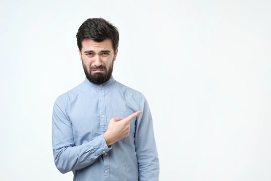 Sad gloomy european boyfriend, whining or crying, frowning and trying to hide tears pointing with finger aside.