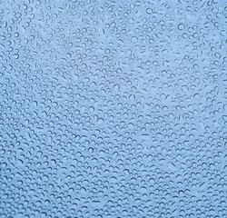 Wassertropfen in runder Form auf Scheibe mit blauem Hintergrund