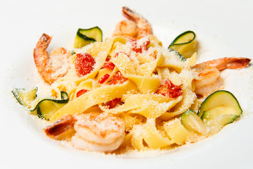 Delicious pasta with shrimps, parmesan, tomatoes and zucchini. White plate background.