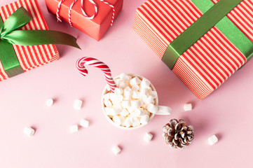 Obraz premium White mug with marshmallows Candy Cane gifts boxes with green ribbon on pink background Flat Lay Winter traditional drink food Festive decor. Christmas New Year presents Xmas holiday