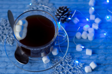 Obraz na płótnie Canvas a Cup of hot coffee with marshmallows on a blue textile background with beautiful Christmas bokeh lights.