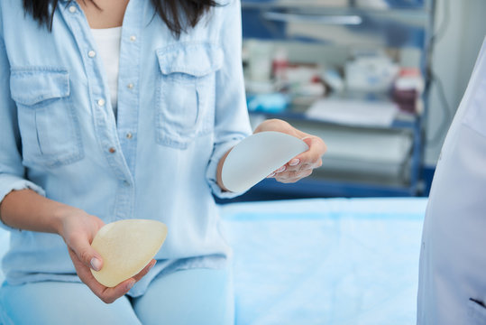 Close up photo of woman holding different types of implants for breast augmentation in doctor office