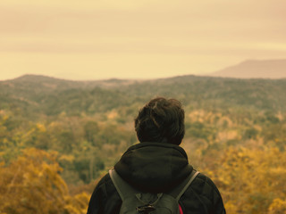 solo backpack and camping concept from backside of black hair man in warm hoodie sweatshirt with his bag solo travel, relax, happy  and see to forest and mountain in morning after sunrise