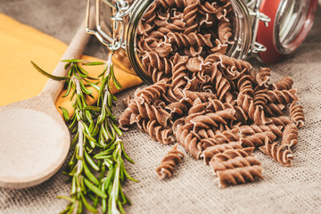 raw whole-grain Italian macaroni of dark color on a linen cloth in the kitchen - rosemary and fusilli