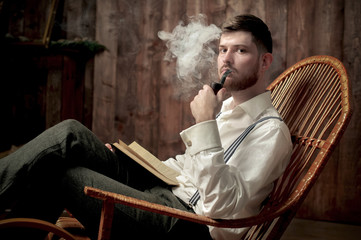 Side view of a stylish young man with suspenders smoking cigar in chair
