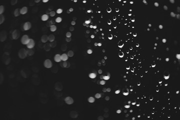 Dirty window glass with drops of rain. Atmospheric monochrome dark background with raindrops in bokeh. Droplets and stains close up. Detailed transparent texture in macro. Copy space. Rainy weather.
