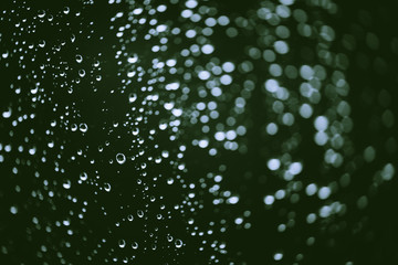 Dirty window glass with drops of rain. Atmospheric green background with raindrops in bokeh. Droplets and stains close up. Detailed transparent texture in macro with copy space. Rainy weather.