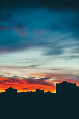 Cityscape with wonderful varicolored vivid dawn. Amazing dramatic multicolored cloudy sky above dark silhouettes of city buildings. Atmospheric background of sunrise in overcast weather. Copy space.