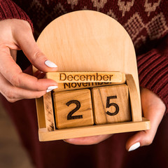 A woman with a white manicure with a bardish sweater holds a wooden calendar which shows the date...