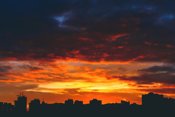Cityscape with wonderful varicolored vivid fiery dawn. Amazing dramatic multicolored cloudy sky. Dark silhouettes of city buildings. Atmospheric background of sunrise in overcast weather. Copy space.