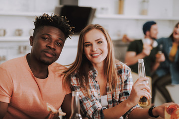 Portrait of charming girl and her friend looking at camera and smiling. They sitting at the table and enjoying beer with pizza