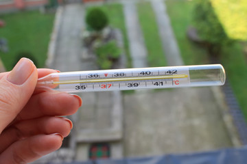 glass mercury thermometer in the hands on the background of the backyard. take measurements of the...