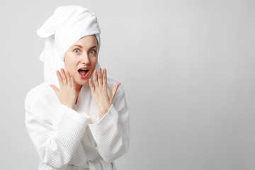 Beautiful girl wearing white bathrobe with towel on the head, looking at camera and smiling, a model with light nude make-up, white studio background, beauty photo, copy space.