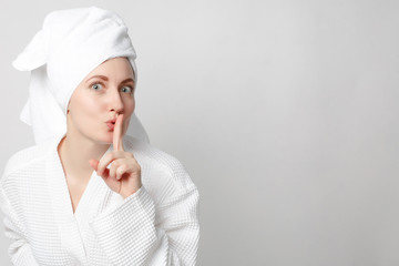 Beautiful girl wearing white bathrobe with towel on the head, looking at camera and smiling, a model with light nude make-up, white studio background, beauty photo, copy space.