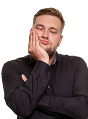 Studio portrait of gloomy european man showing boredom while leaning head on hand and standing over white background.