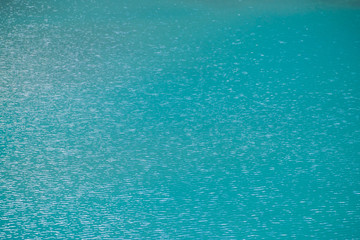 Amazing textured background of calm azure clean water surface. Sunshine in mountain lake close up. Beautiful ripples on shiny water in sunny day. Wonderful relax texture.