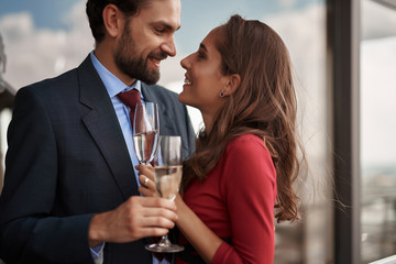 Concept of happy romantic date. Waist up portrait of cheerful beloved couple with champagne glasses looking with love and passion to each other
