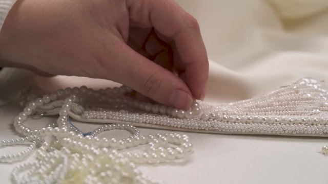 A closeup of woman's hand matching three pearl strings to a beaded lace on the wedding dress and choosing the best one to embellish