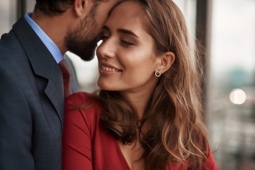 Concept of romantic date. Close up portrait of happy beloved lady clinging with love to her male lover while standing in his arms on balcony