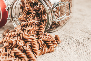 Fototapeta na wymiar Dark brown whole grains of pasta in a glass jar in the kitchen on a wooden table