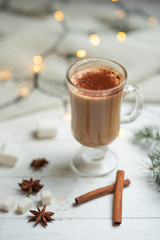 Coffee with milk, latte, hot chocolate with cinnamon sticks and anise stars with white chocolate and marshmallow, with a Christmas tree branch on a bright white background, with lights from a garland