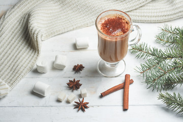 Coffee with milk, latte, hot chocolate with cinnamon sticks and anise stars with white chocolate and marshmallow, with a Christmas tree branch on a bright white background, with lights from a garland