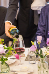 Pouring red wine from bottle into glass at the Party table decorated with beautiful flowers