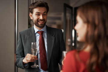 Concept of romantic date and celebration. Waist up portrait of happy gentleman with champagne glass looking at young smiling lady