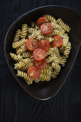 Bowl of fusilli served with basil pesto sauce and fried cherry tomatoes, vertical shot, top view