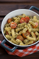 Bowl of fusilli pasta with green basil pesto and roasted tomatoes, vertical shot, close-up