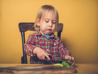Little toddler cutting avocado at table