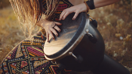 Beautiful young hippie woman with dreadlocks playing on djembe. Funky woman drumming in nature on...
